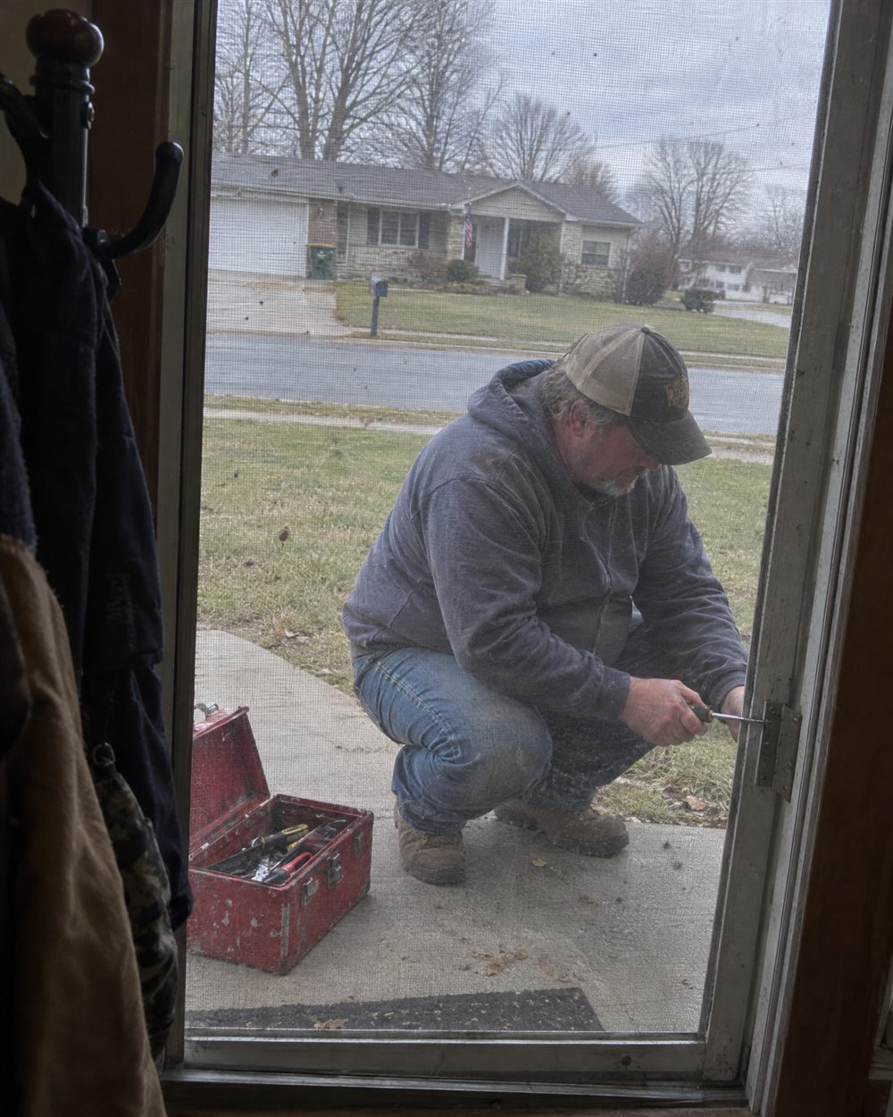 Man kneeling by his toolbox, seen through the front door