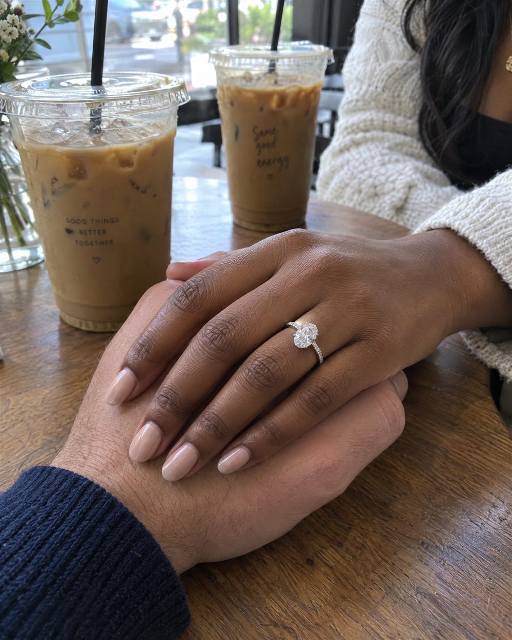 Holding hands across a café table, engagement ring on her finger
